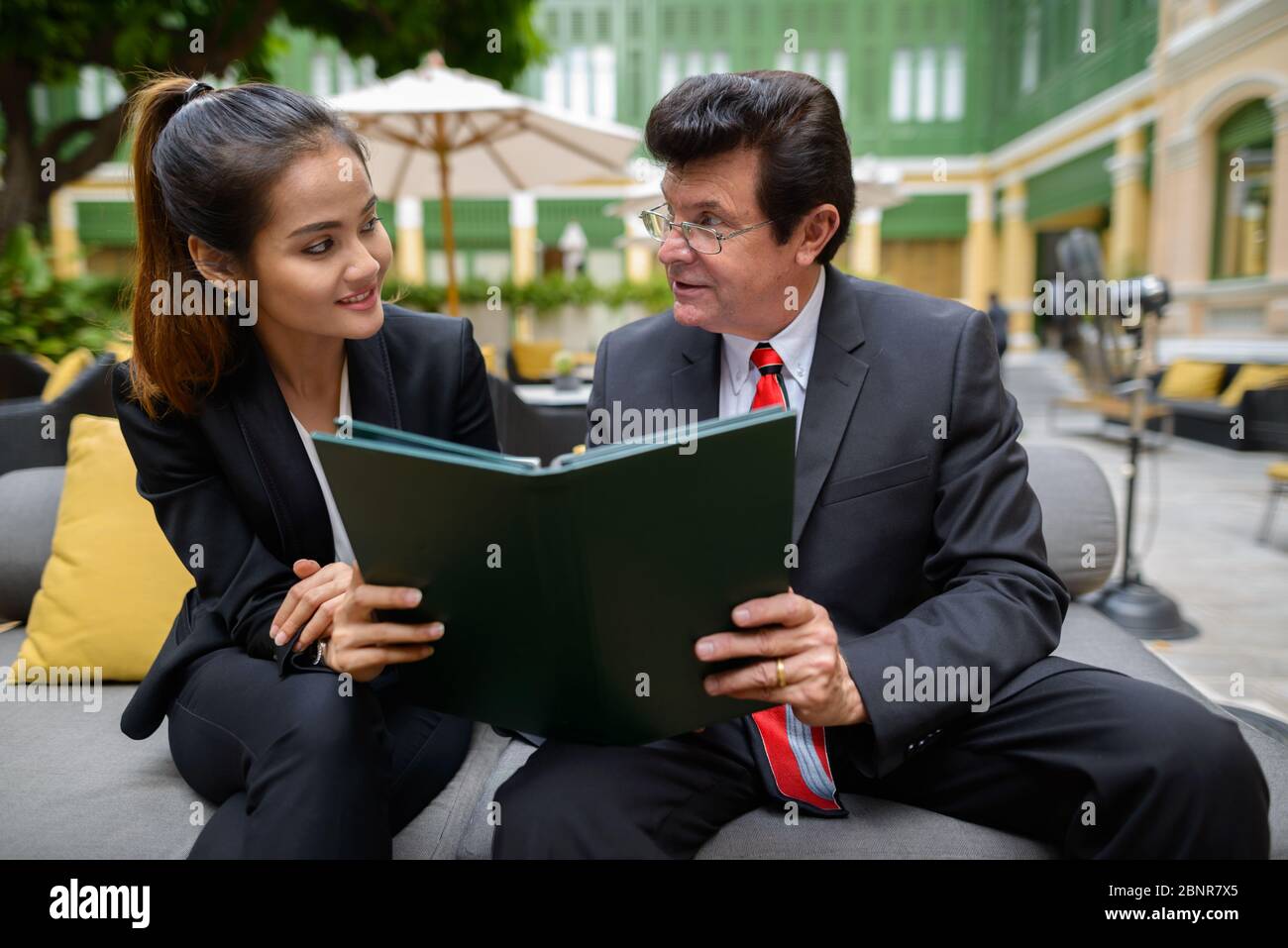 Happy mature businessman and young Asian businesswoman reading the menu together Stock Photo