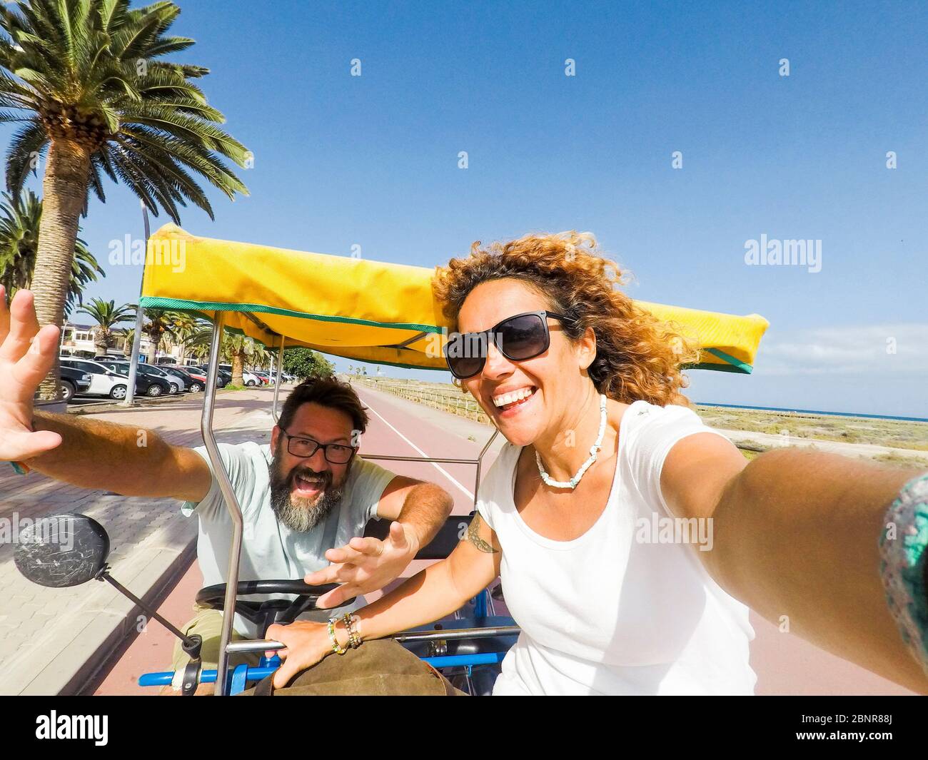 Happy and cheerful adult beautiful couple enjoying the outdoor leisure actvity on vacation with rented funny bike together laughing a lot and having fun Stock Photo