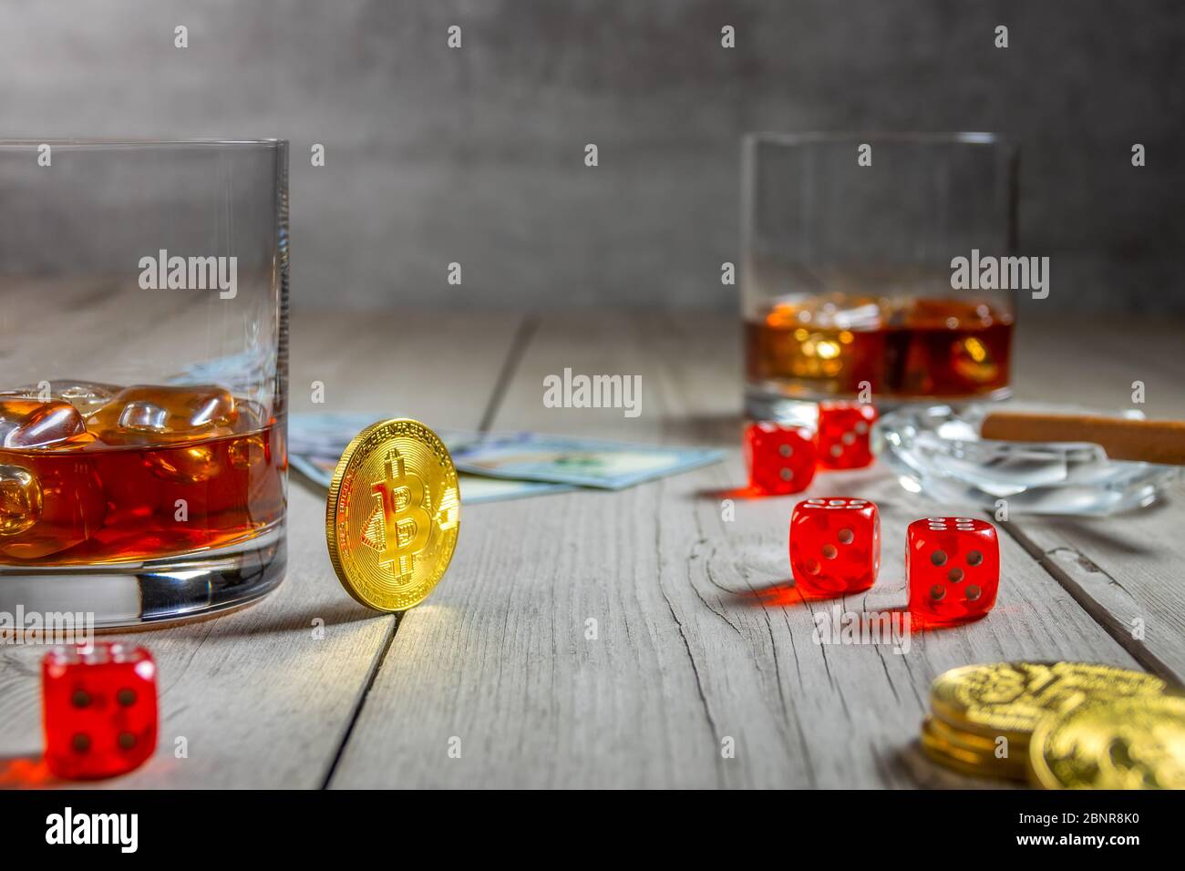 Rustic wooden table. Two glasses of whiskey with ice cubes and a cigar in an ashtray. Dice and dollar bills. Few bitcoin coins Stock Photo