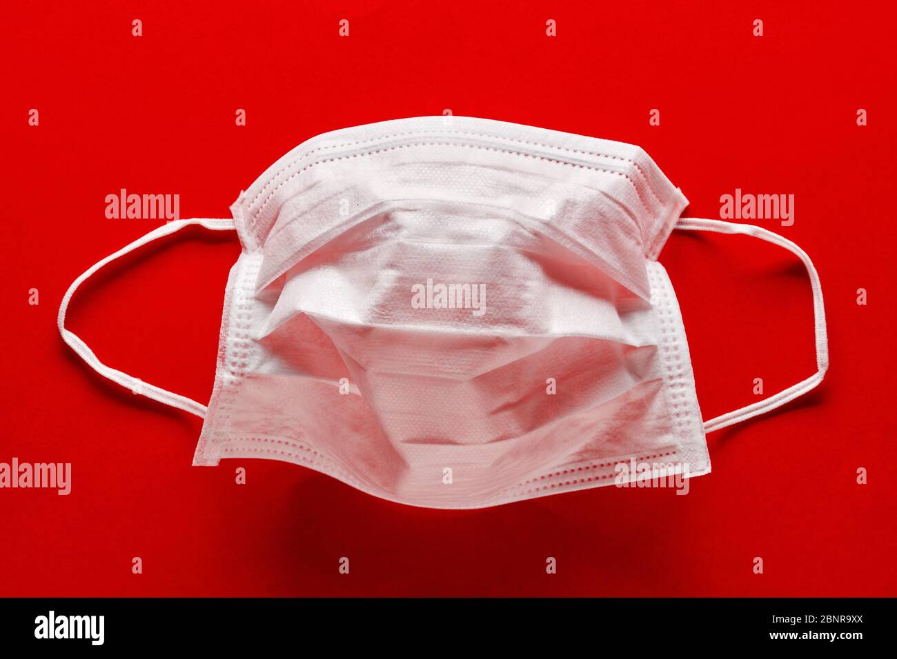 Medical or surgical mask for protection against virus diseases on red background. COVID-19 or corona virus protection. Stock Photo