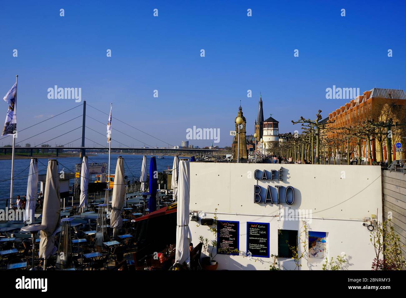 Sunny afternoon at the Rhine river promenade, a popular tourist attraction. Cafe exterior in foreground, white historic castle tower in background. Stock Photo