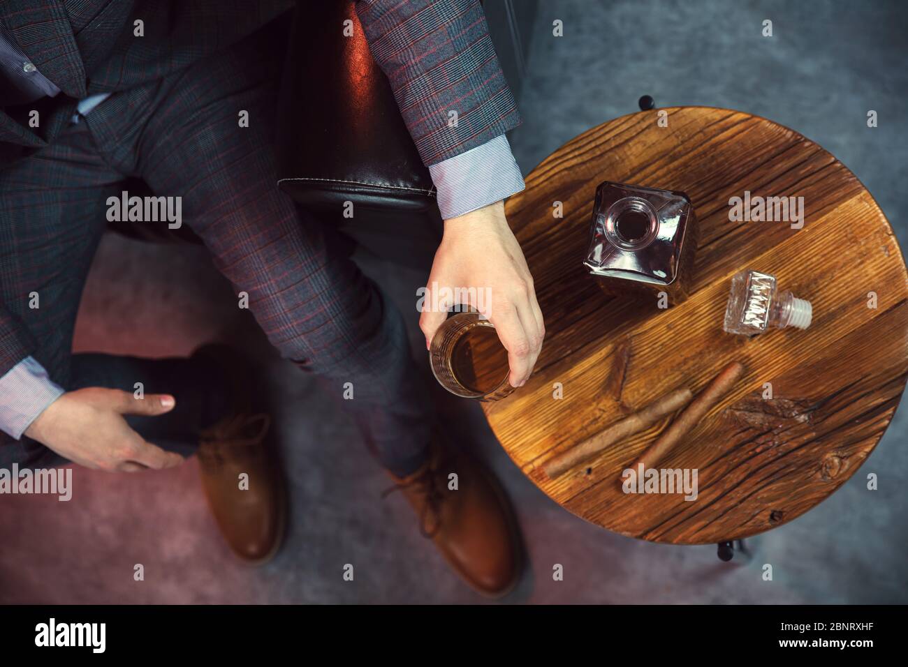 Gentleman takes a glass of whisky and a wooden table with carafe of whisky and cigars. View from the top. Stock Photo