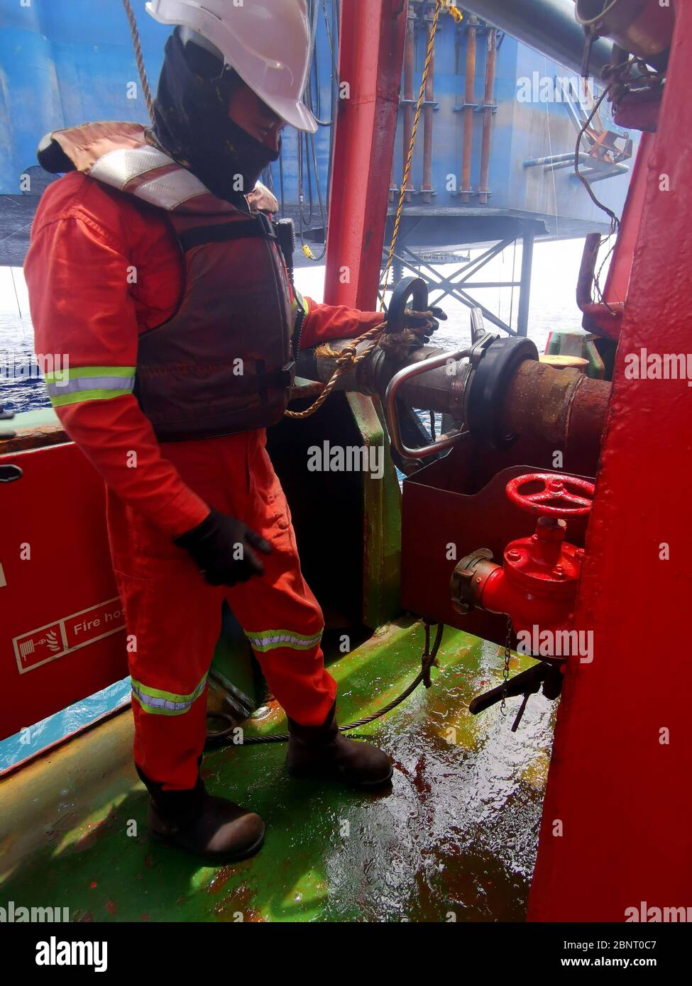 Marine crew disconnected cargo hose on deck wearing correct PPE Stock Photo