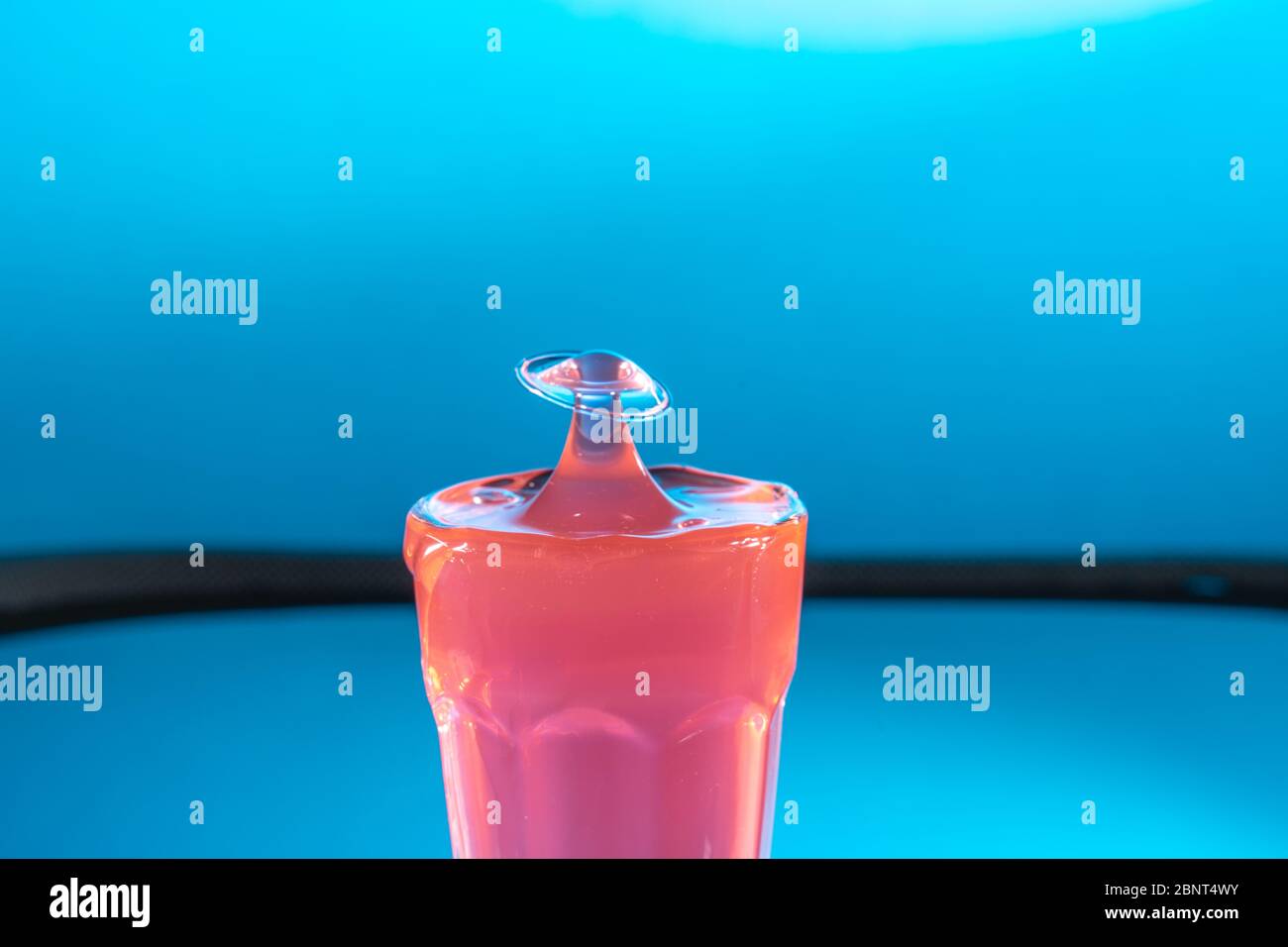 Pink liquid drop falls into glass, hitting liquid surface,forms mushroom shape. Selective focus Stock Photo