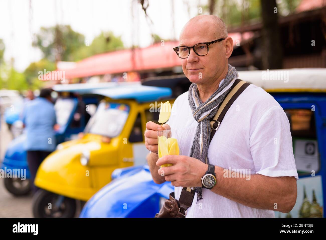 Portrait of senior tourist man eating sliced mangoes in Ayutthaya Stock Photo
