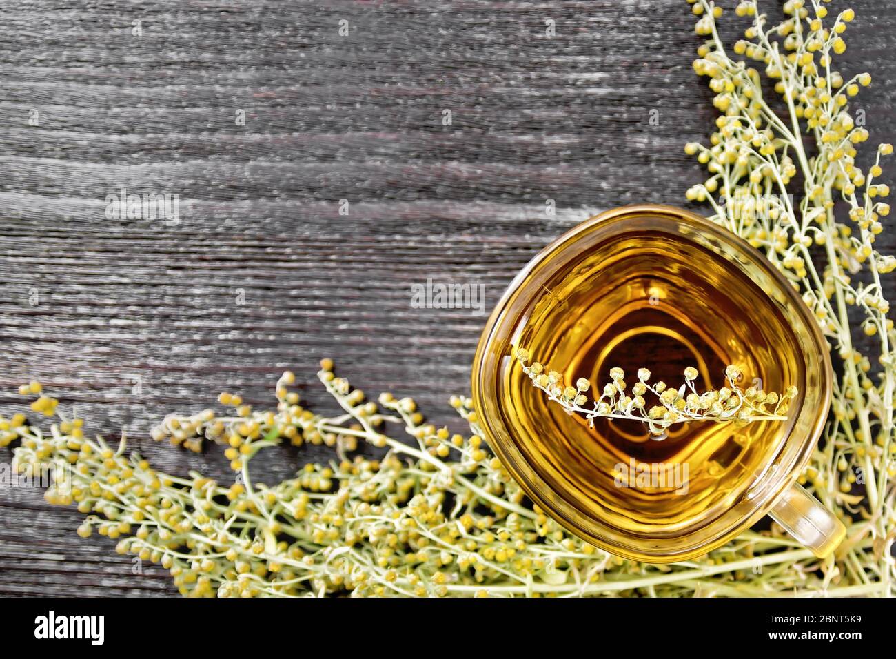 Gray wormwood herbal tea in a glass cup, fresh sagebrush flowers on wooden board background from above Stock Photo