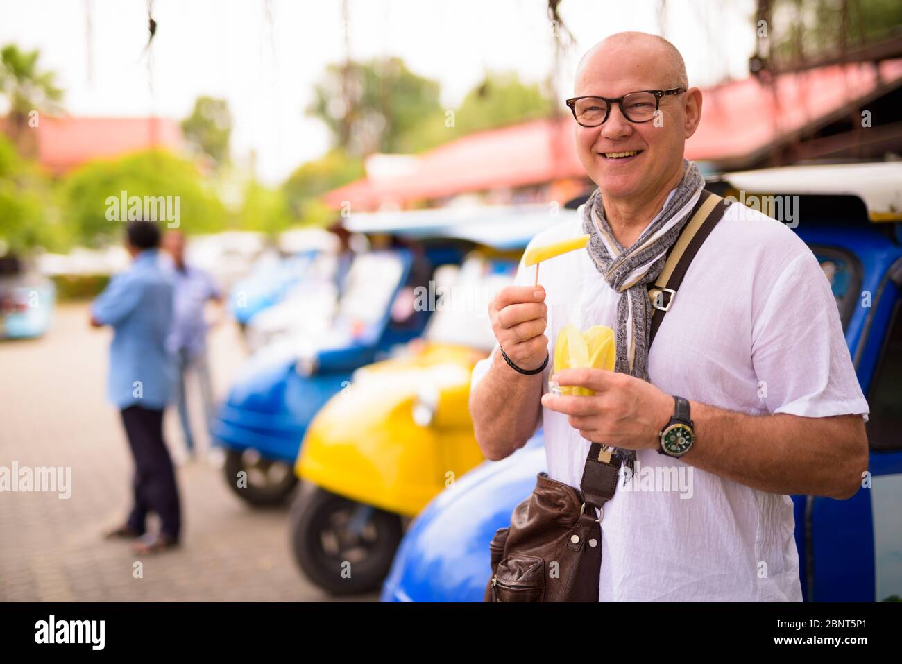 Portrait of happy senior tourist man eating sliced mangoes in Ayutthaya Stock Photo