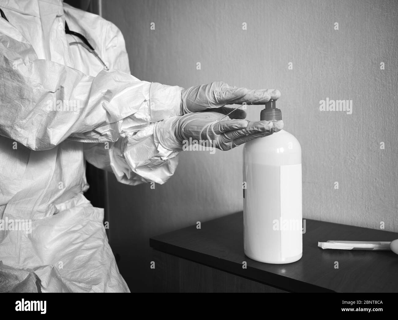 Black and white cropped image of doctor in PPE suit, gloves, decontaminating hands with alcohol sanitizer. Preventive measures against coronavirus. COVID-19 concept Stock Photo