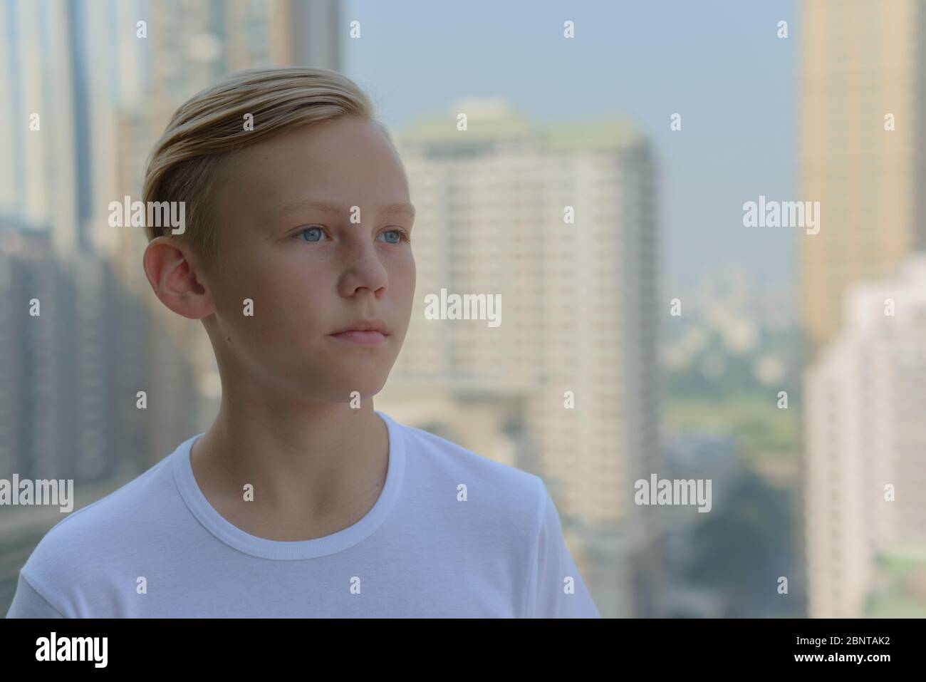 Face of young handsome boy with blond hair thinking against view of the ...