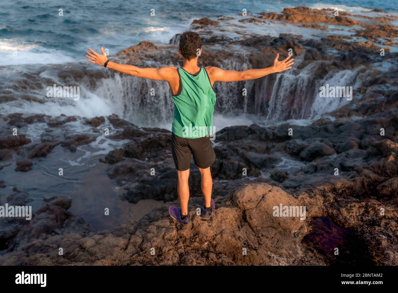 close up. young man is standing in front of a rock formation and raises his arms in admiration to see how the water disappears into the hole Stock Photo