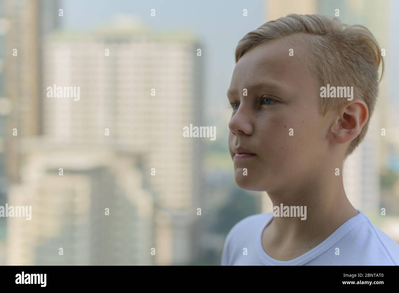 Face of young handsome boy with blond hair thinking against view of the ...