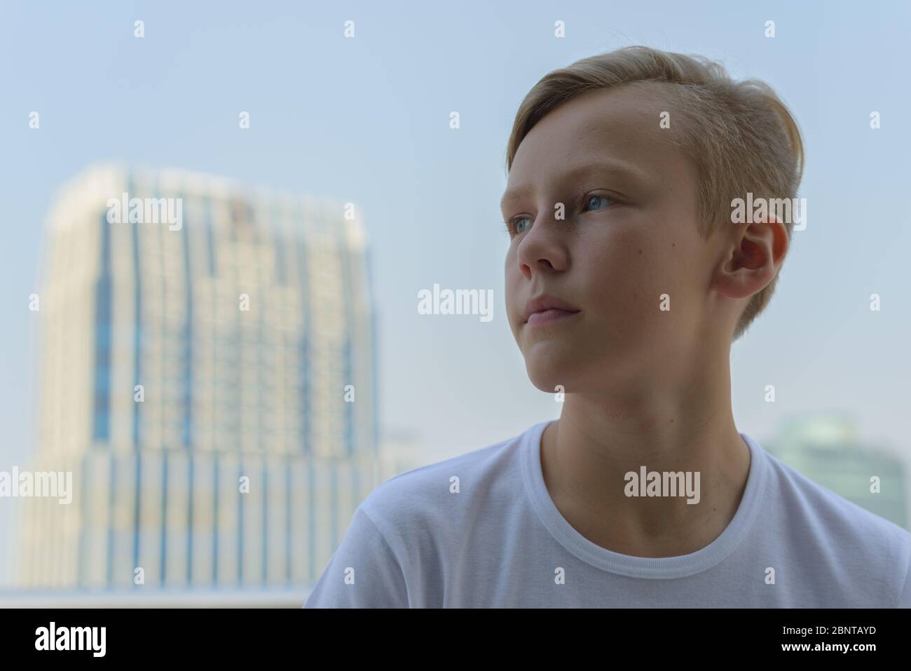 Face of young handsome boy with blond hair thinking against view of the ...