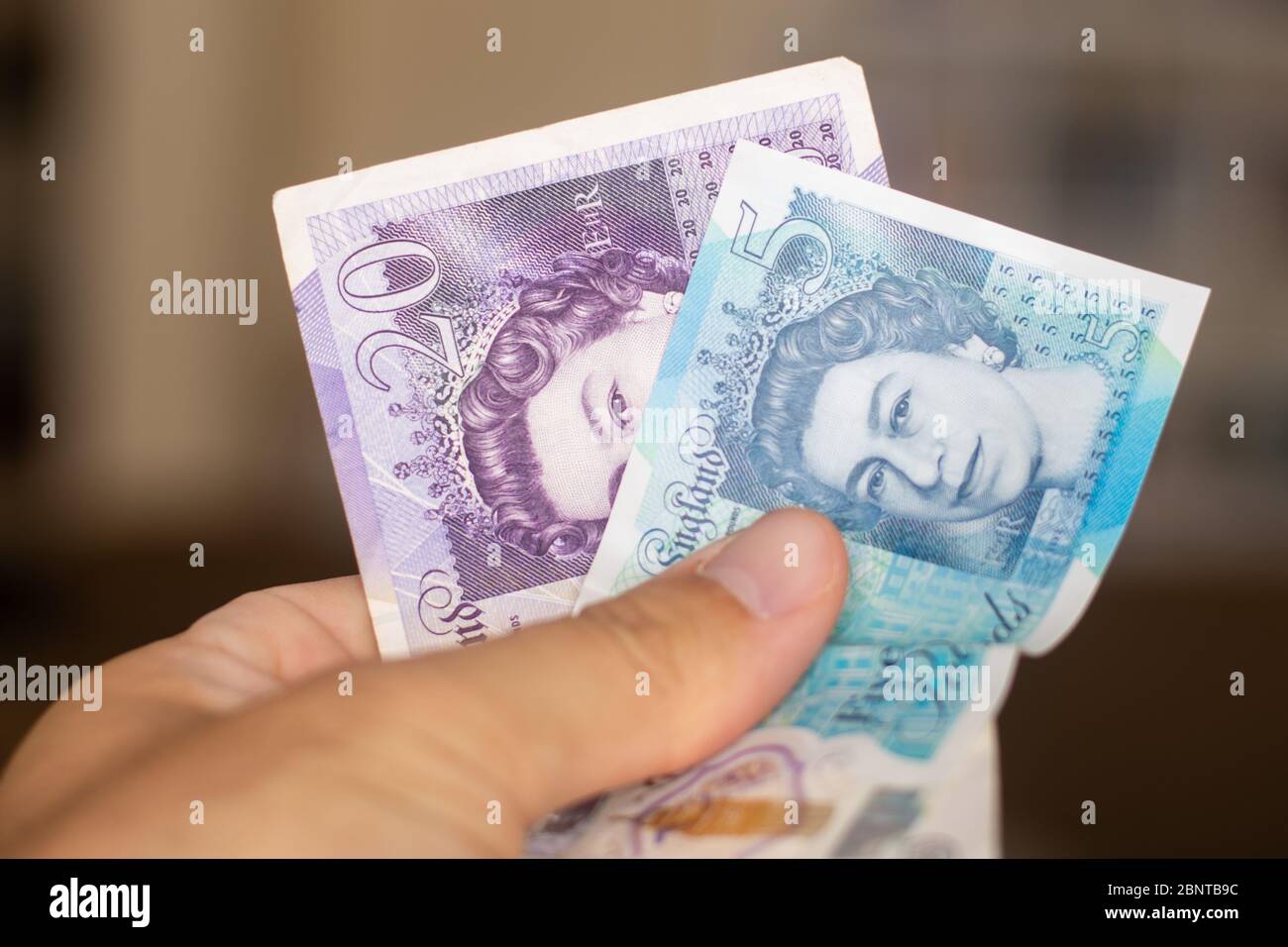 Persons hand giving the Currency of the England in the United Kingdom - One purple twenty pound and blue five pound note spread out on a brown backgro Stock Photo