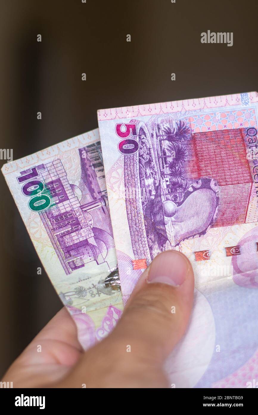 Persons hand giving the Currency of the Qatar One fifty and hundred