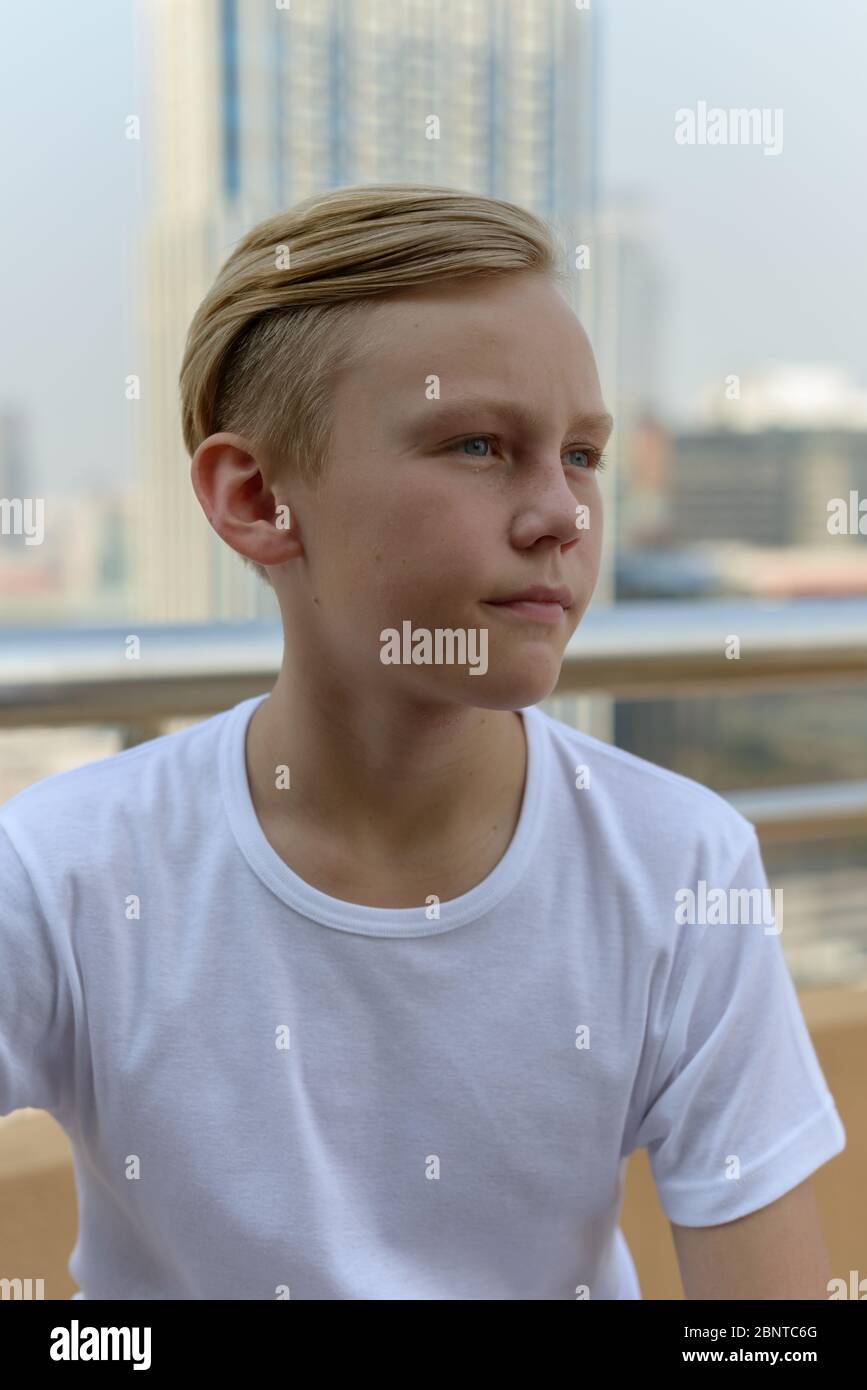 Young handsome boy with blond hair thinking against view of the city ...