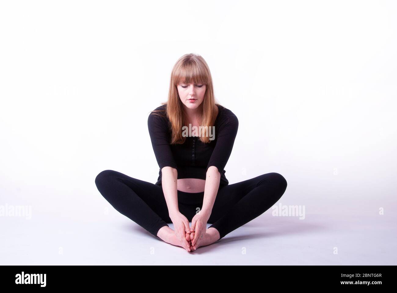 A young pregnant woman sitting crosslegged on the floor practicing