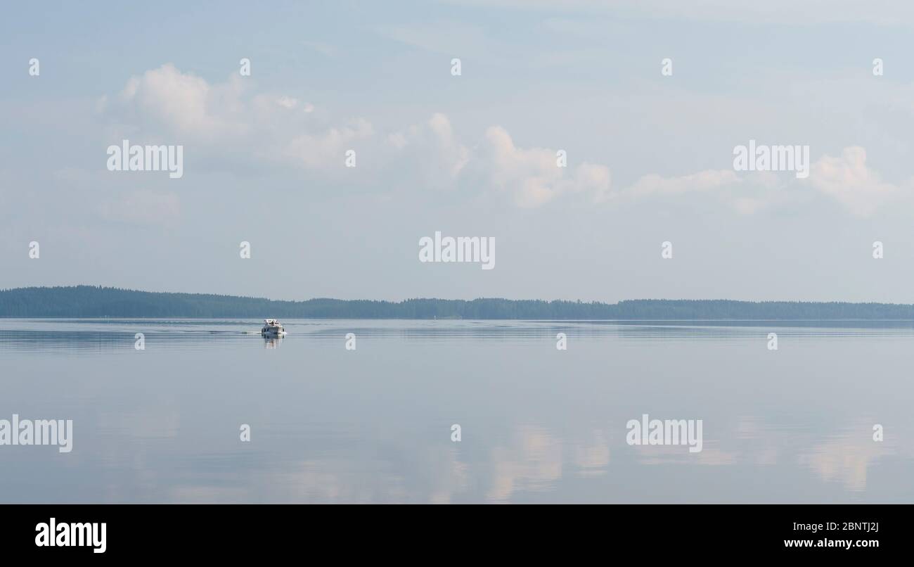 Travelers at distant motorboat at calm Lake Pohjois-Konnevesi at Summer , Finland Stock Photo