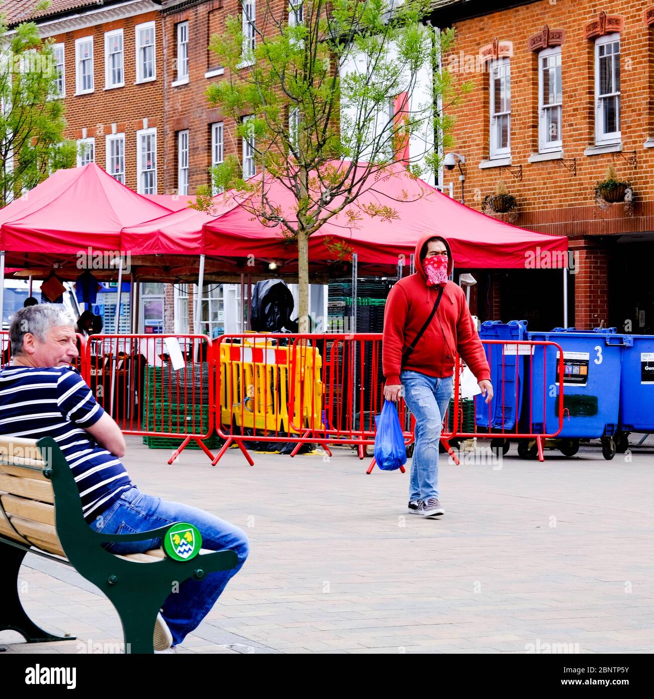A Pedestrian Walking With Shopping Wearing A Homemade Protective Face Mask Passing A Man On A Bench With No Protection Stock Photo