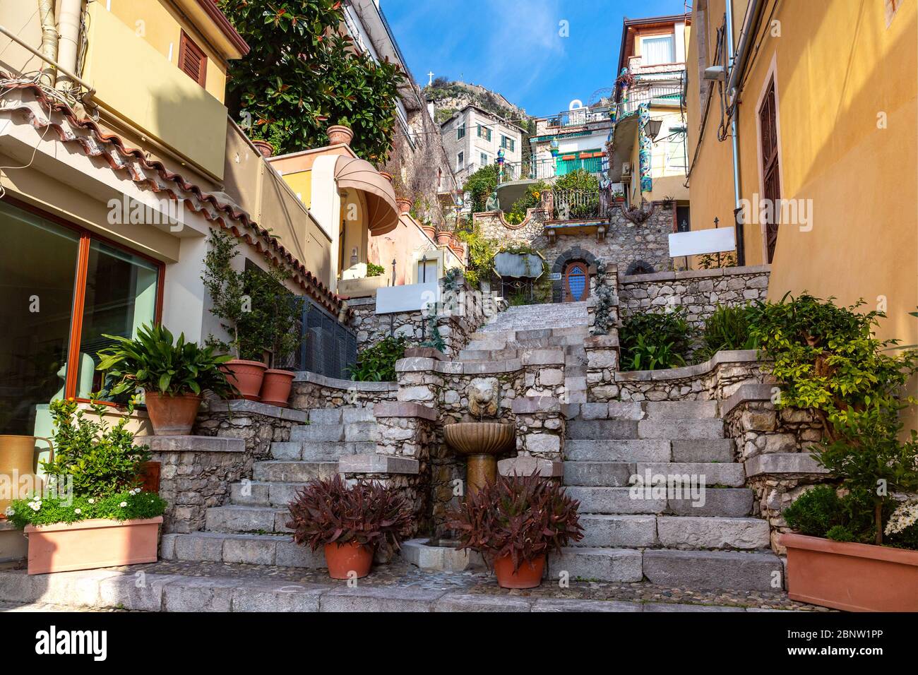 Colorful narrow stairs street with Fountain and flowers near square Piazza Duomo in Taormina in sunny morning, Sicily, Italy Stock Photo