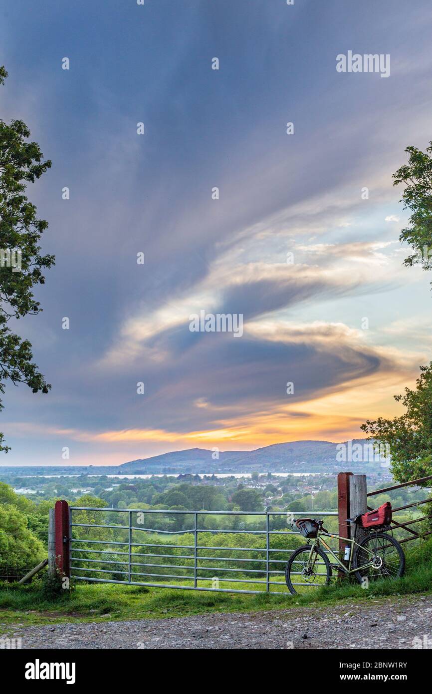 A bike leans against a gate overlooking the cheddar reservoir with the mendip hills and dramatic clouds forming the backdrop (portrait format) Stock Photo