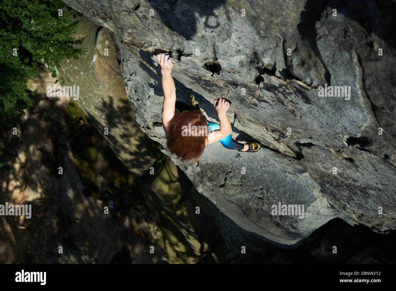 Horizontal snapshot of red haired woman in safety harness, climbing up the rock. Top view. Extreme sport concept Stock Photo