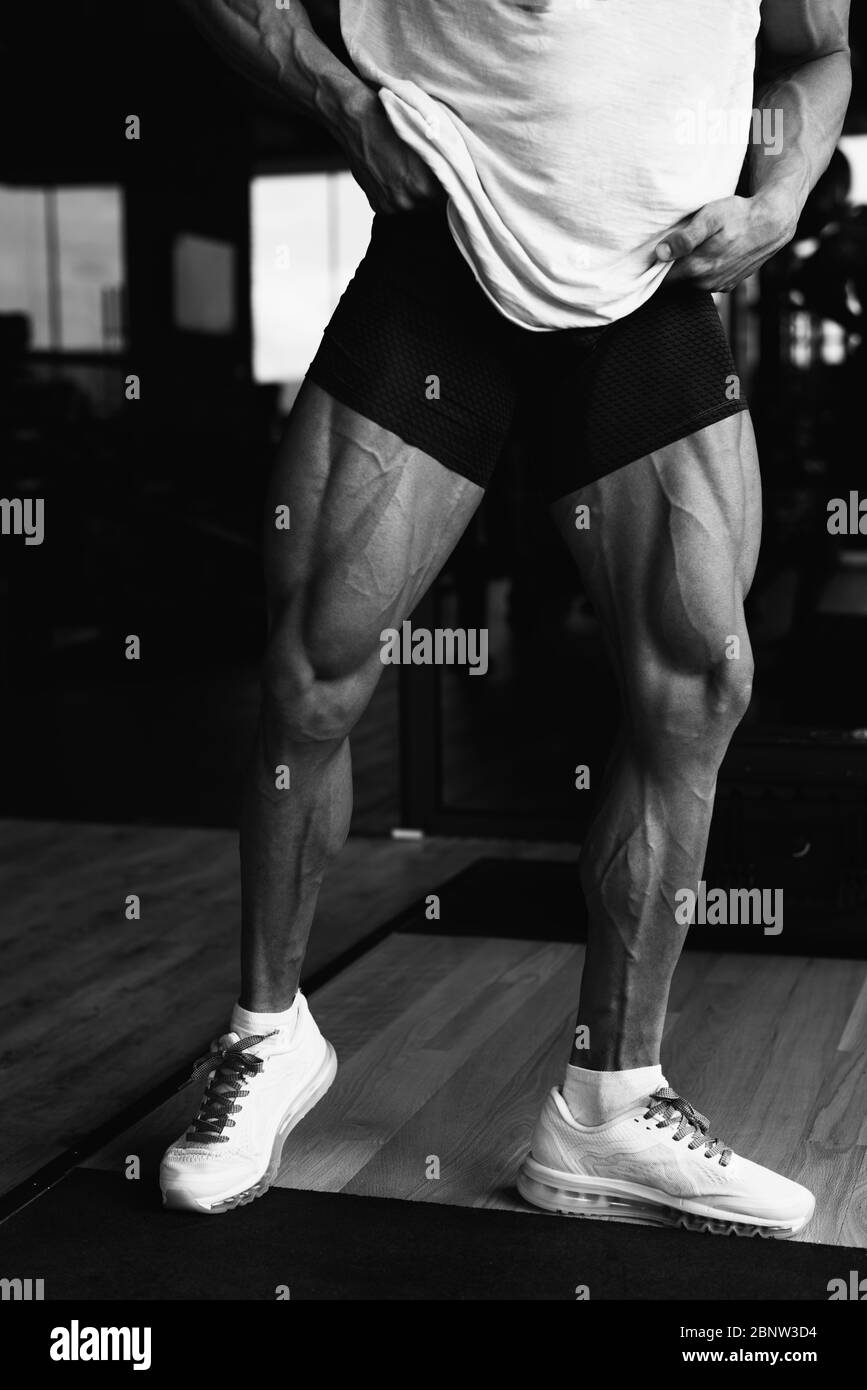 Healthy Young Man Standing Strong in the Gym and Flexing Legs Close Up - Muscular Athletic Bodybuilder Fitness Model Posing After Exercises Stock Photo