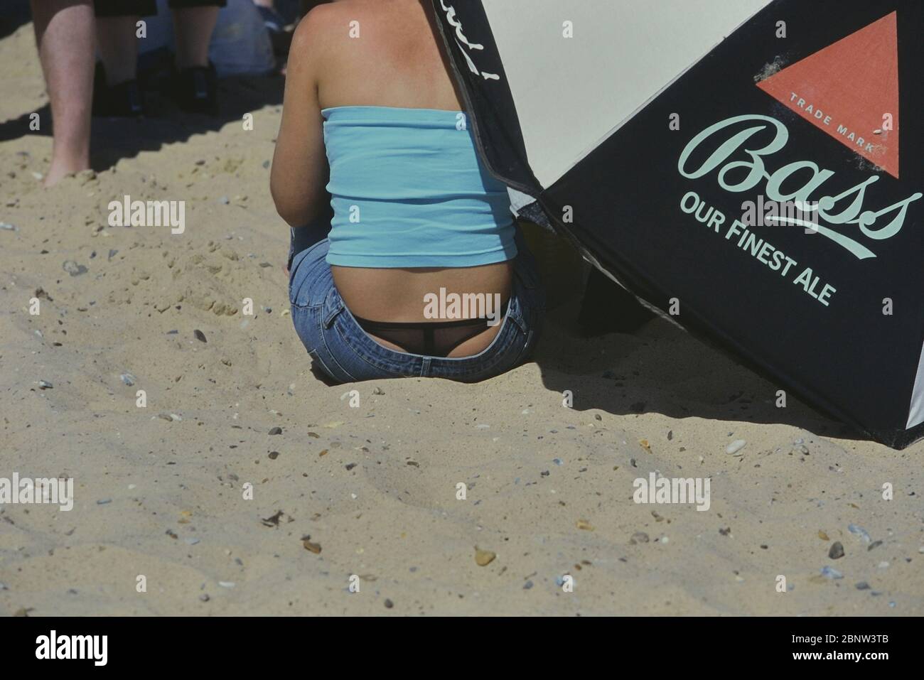 Woman sitting on the beach showing a her G-string, thong or Whale tail  above the rim of low rise jeans. Great Yarmouth, Norfolk, England, UK.  Circa 1990's Stock Photo - Alamy