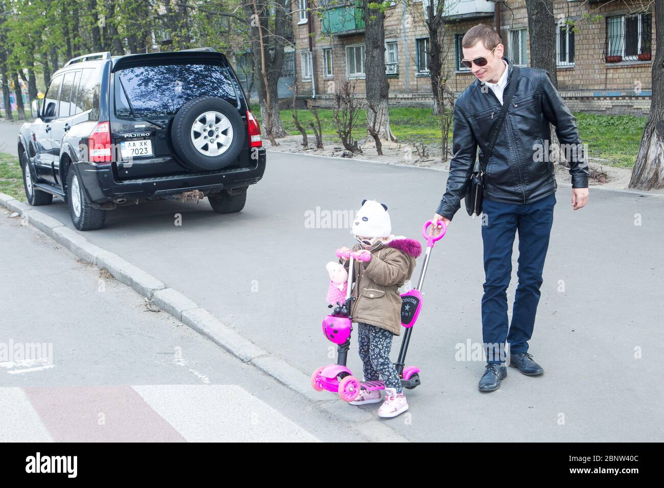 Young father leads little child on pink scooter to the pedestrian crossing on the street in Kiev to safely make his way to the other side Stock Photo