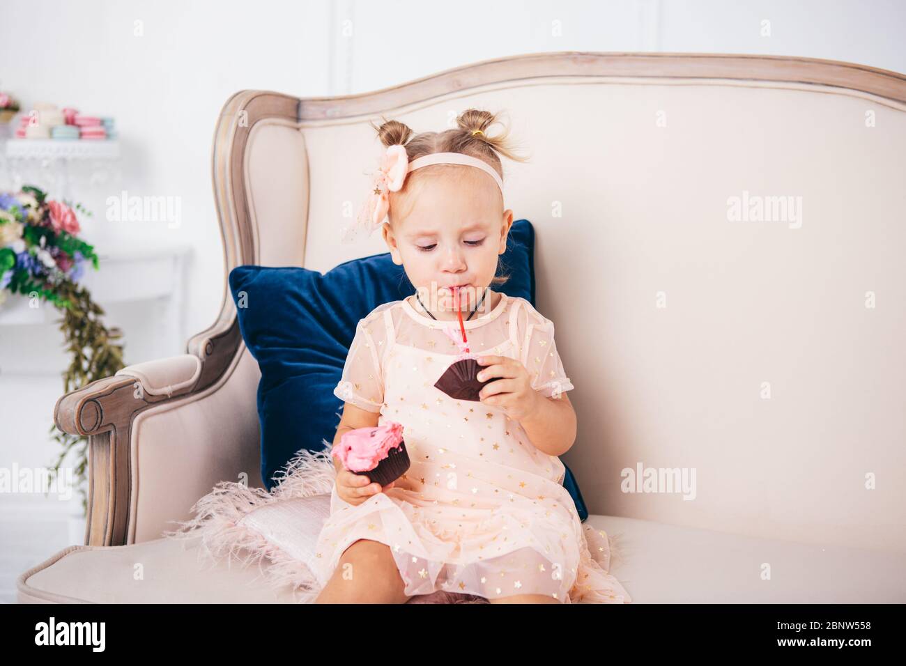 Little child girl in beautiful dress eats cake while sitting on sofa in ...