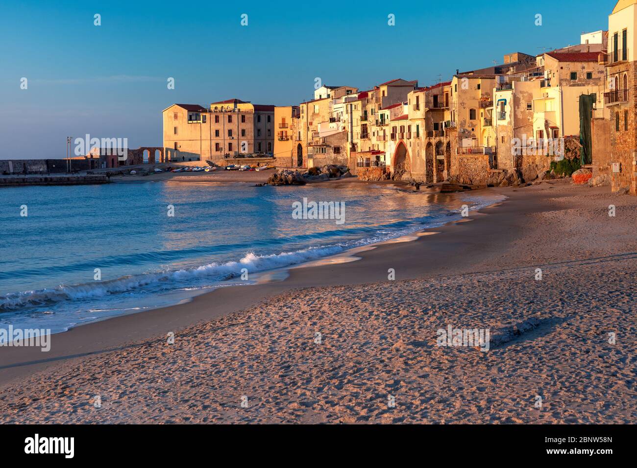 Beautiful view of empty sunny sand beach and old town of coastal city Cefalu at sunset, Sicily, Italy Stock Photo