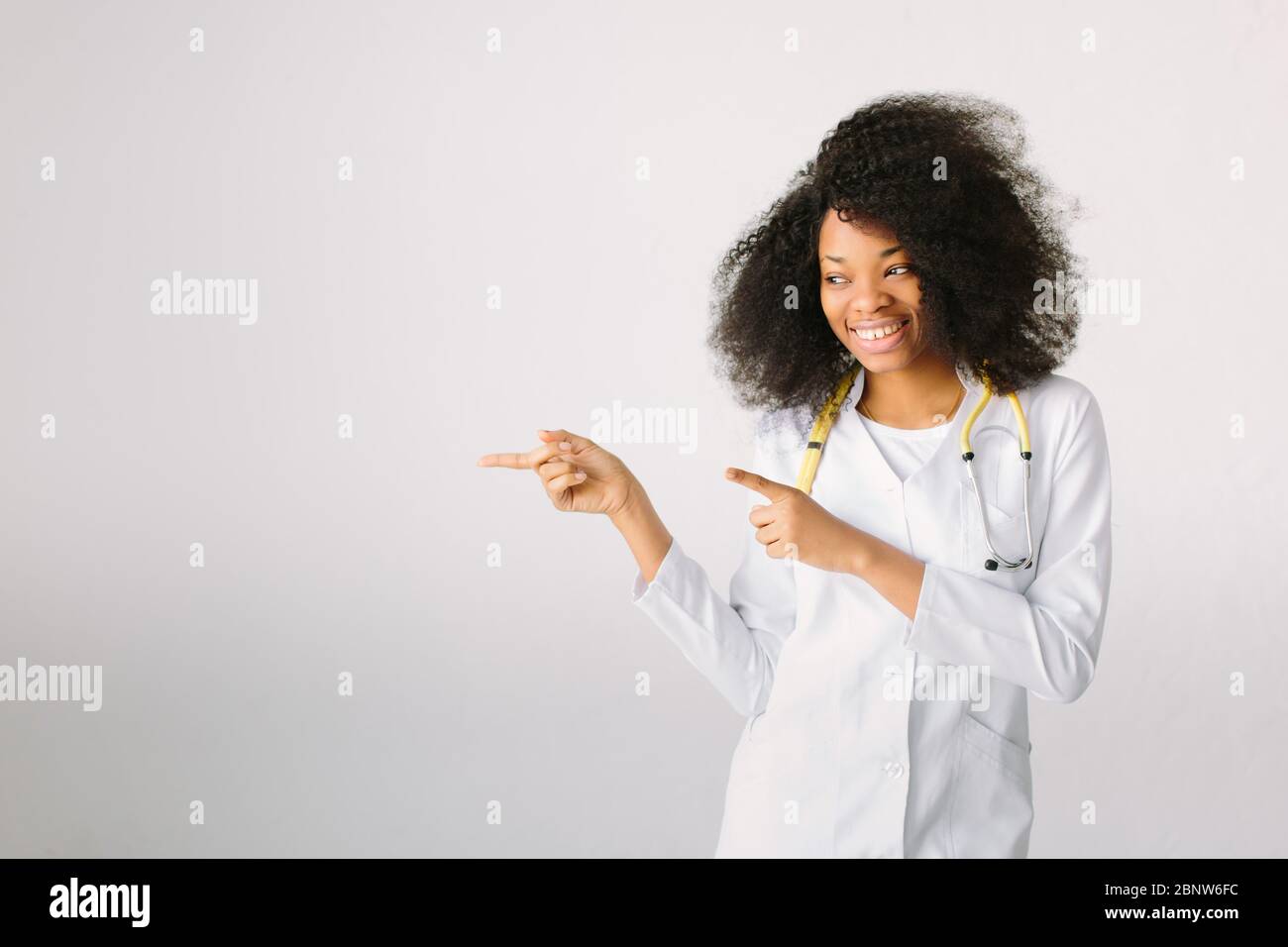 Beautiful African American doctor or nurse smiling isolated over white background, show something important. Stock Photo