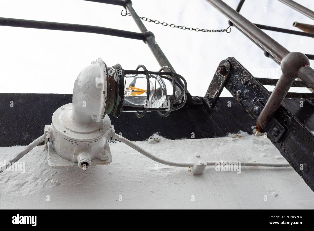 Vintage caged metal light fixture on the exterior of an old ship vessel, heavy paint, horizontal aspect Stock Photo