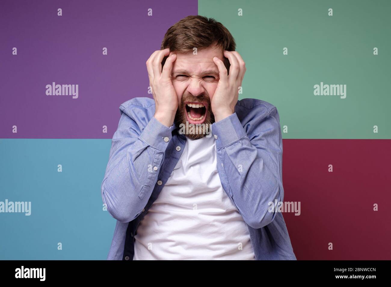 Caucasian bearded man in stress, he screams and grabs his head with hands. Stock Photo