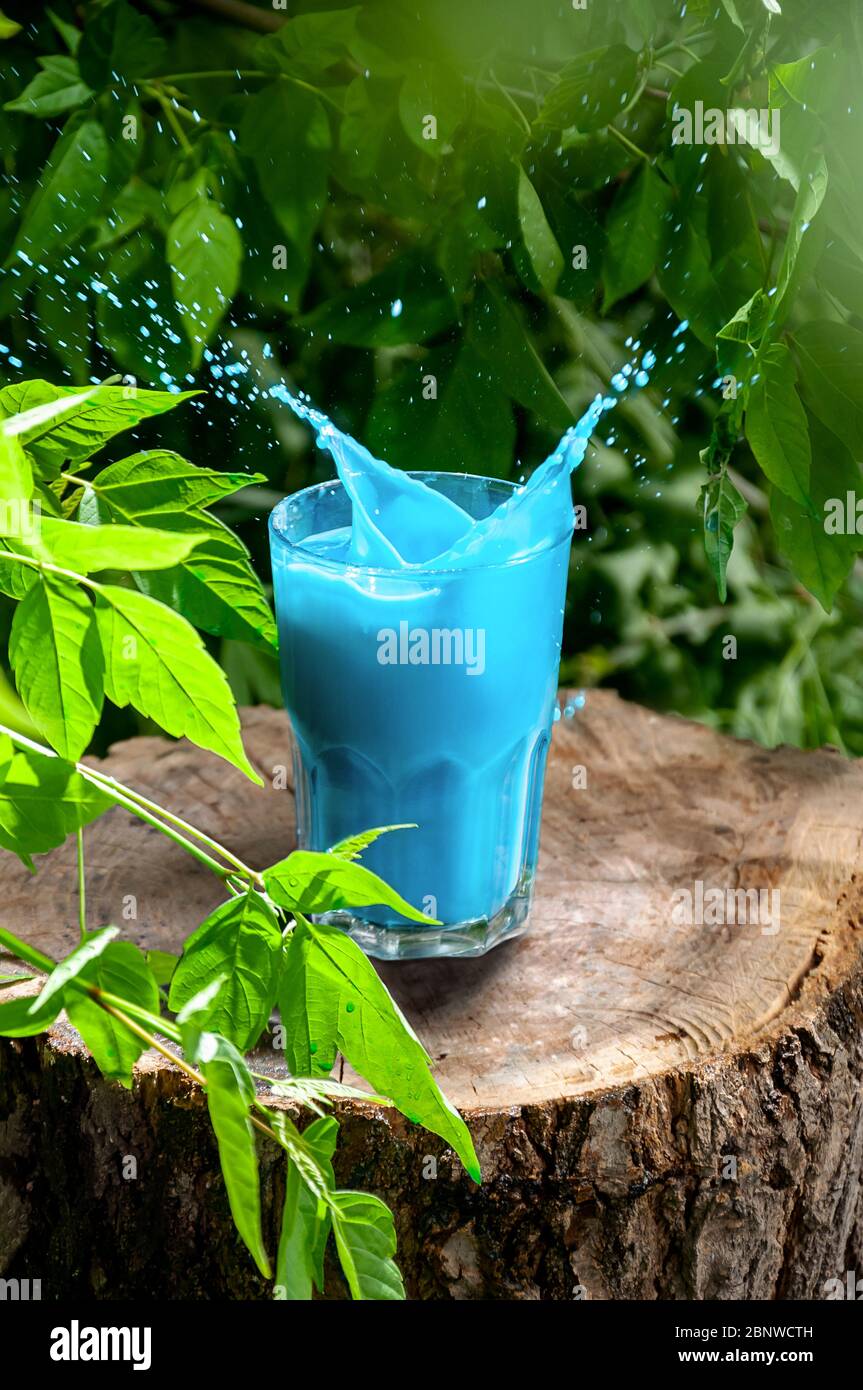 Blue Hawaii Cocktail in Glass with Splash on Wooden Stump in Forest. Refreshing Summer Drink Concept. Stock Photo