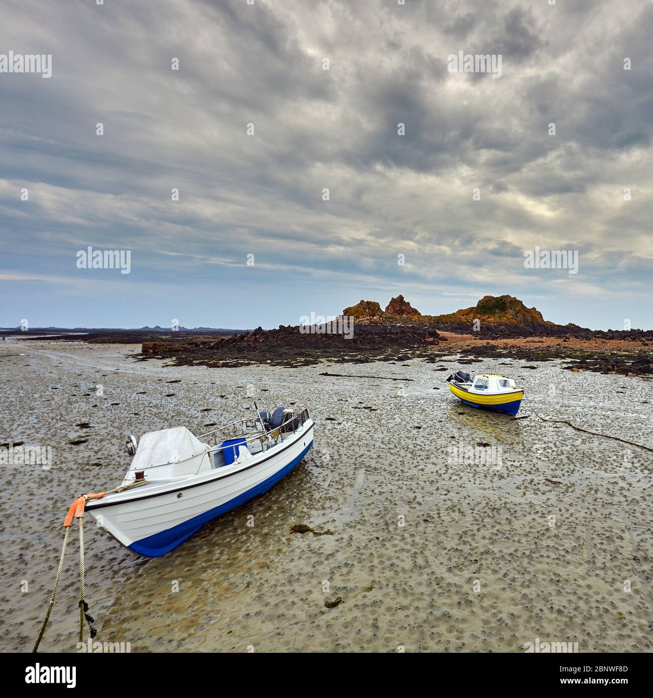 Image of small fishing boats dried out on the beach with rocks sand and cloudy sky. Le Hocq, St