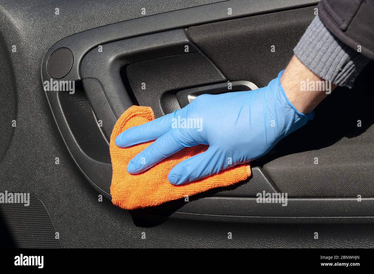 Hand of driver in blue protective glove is wiping with a cloth an interior handle of car door. Coronavirus or Covid-19 car disinfection Stock Photo