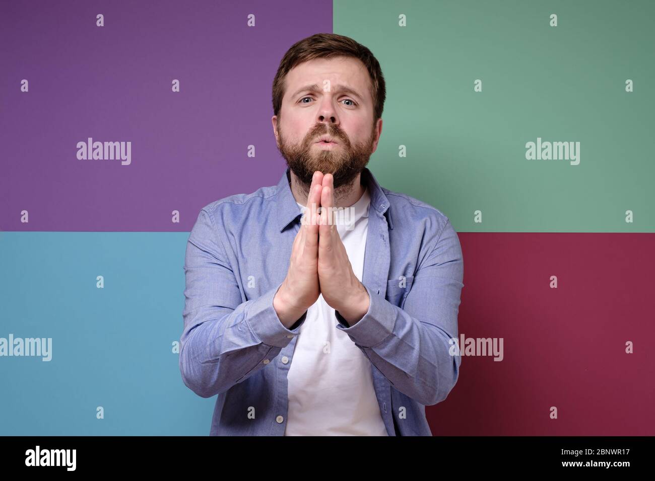 Cute, Caucasian man with a pleading expression on face clasped hands and looks with pitiful eyes. Stock Photo