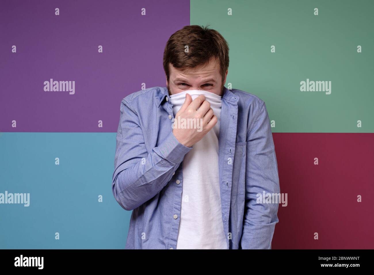 Man feels a fetid odor, he covered his nose with a t-shirt, squinted eyes in displeasure, and squeezed his shoulders. Stock Photo