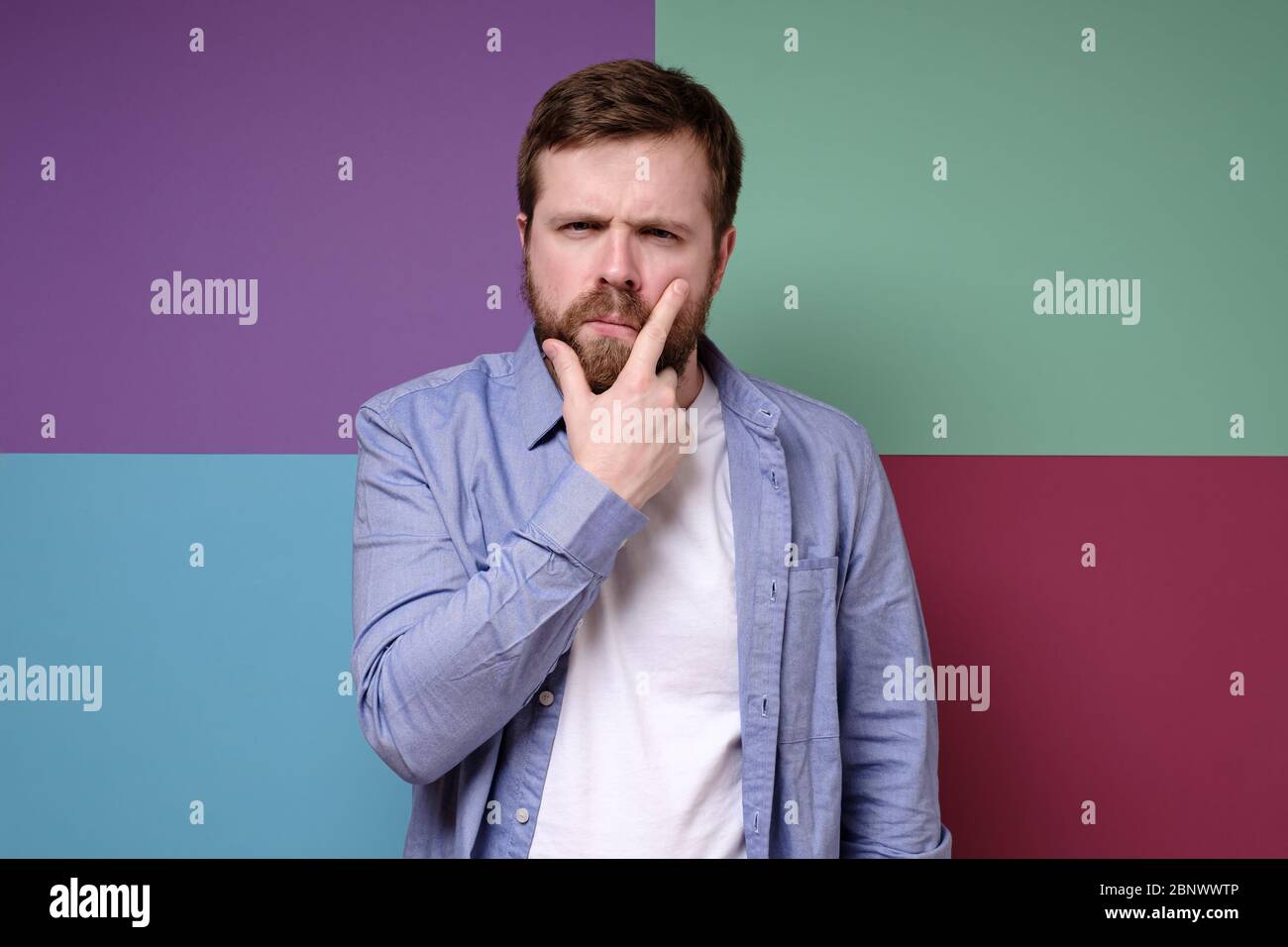Pensive attractive bearded man with a suspicious look holds hand on face. Stock Photo