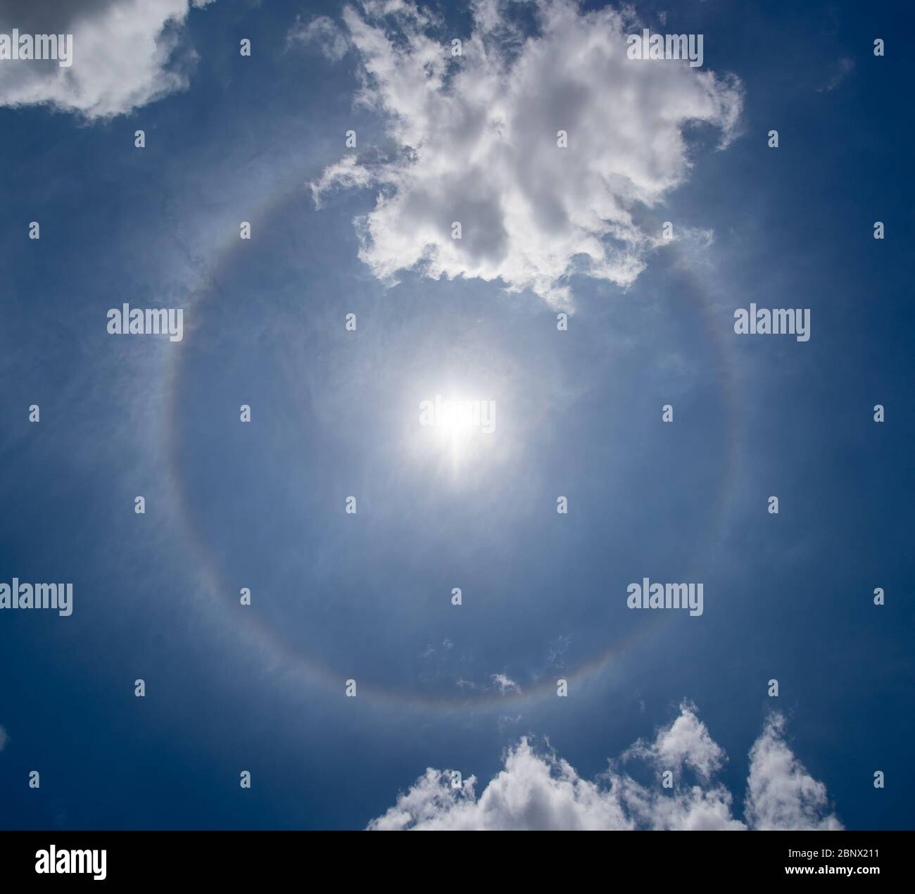 Photo of a solar halo visible in the sky. A color circle with the sun in the center and some cirrus clouds around it Stock Photo
