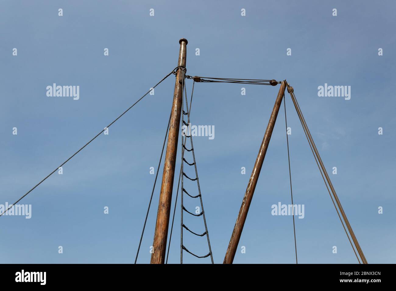 Metal topped wooden mast with simple shroud and rigging against a blue ...