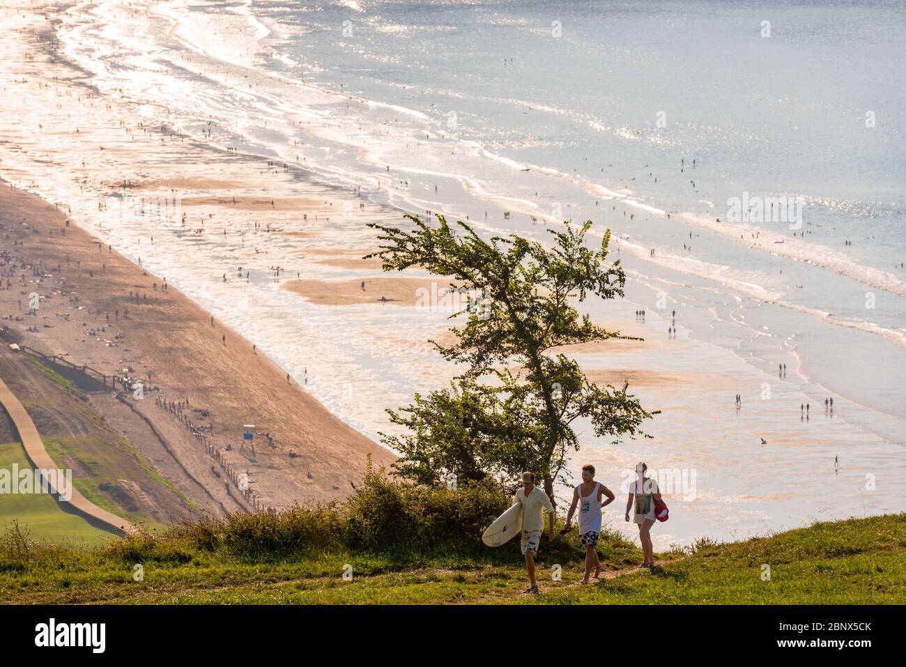 A group of young people with a surfboard returns to the campsite at Zarautz beach Stock Photo