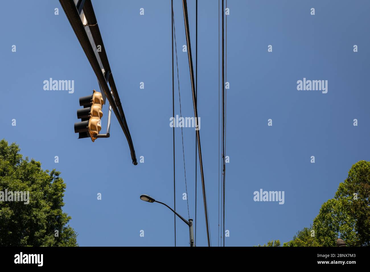 Overhead mast arm with traffic light, power lines and street light against blue sky with trees on lower border, horizontal aspect Stock Photo