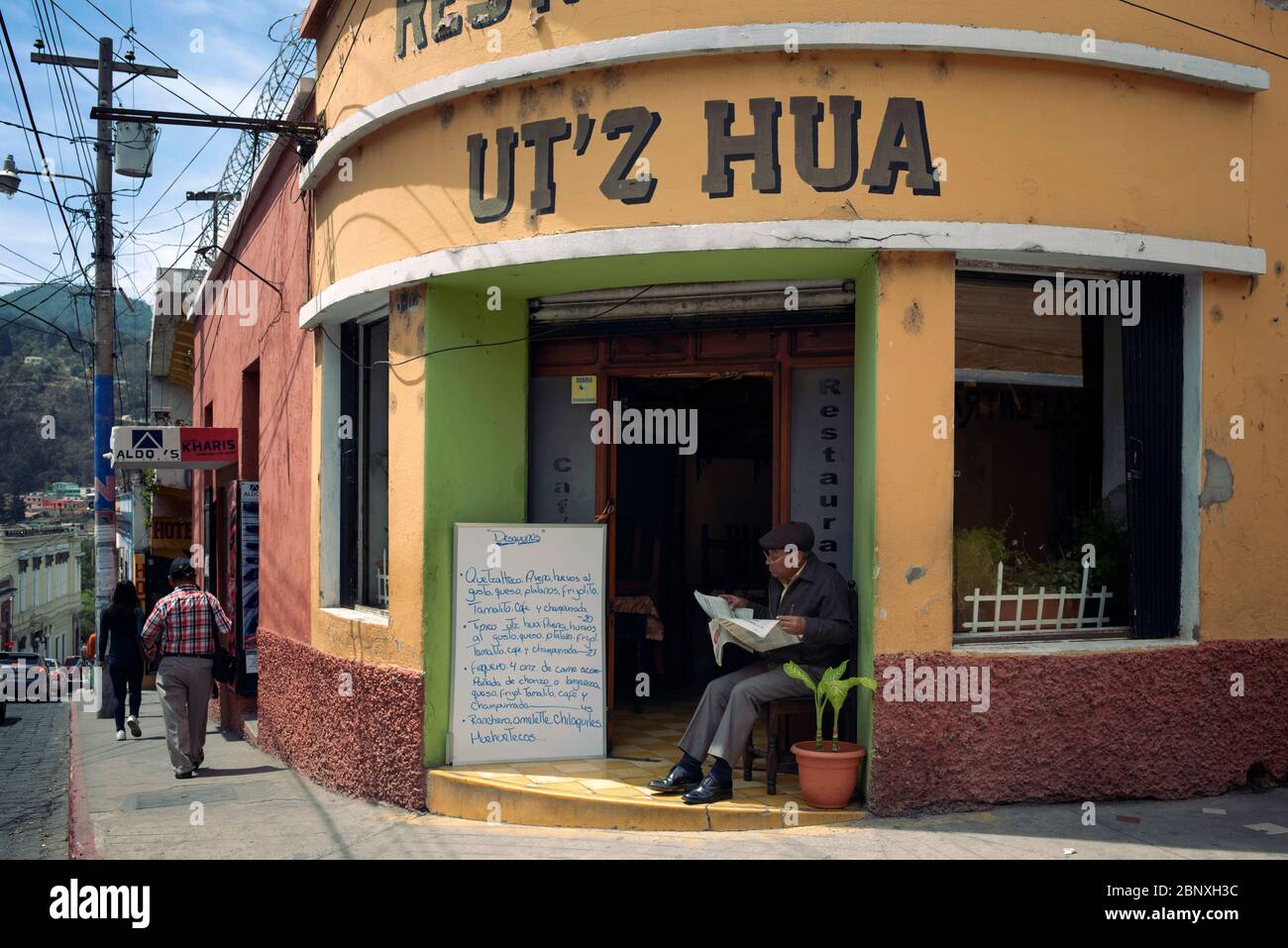 Latino man with newspaper outside Ut'z Hua local restaurant. Mayan eatery offering homemade meals, daily specials. Quetzaltenango, Guatemala. Mar 2019 Stock Photo