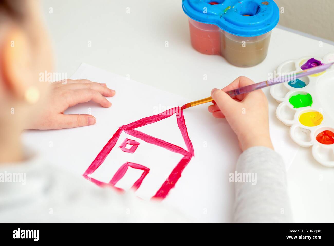 The hand of child drawing a house roof on white paper. Concept of creative learning. Stock Photo