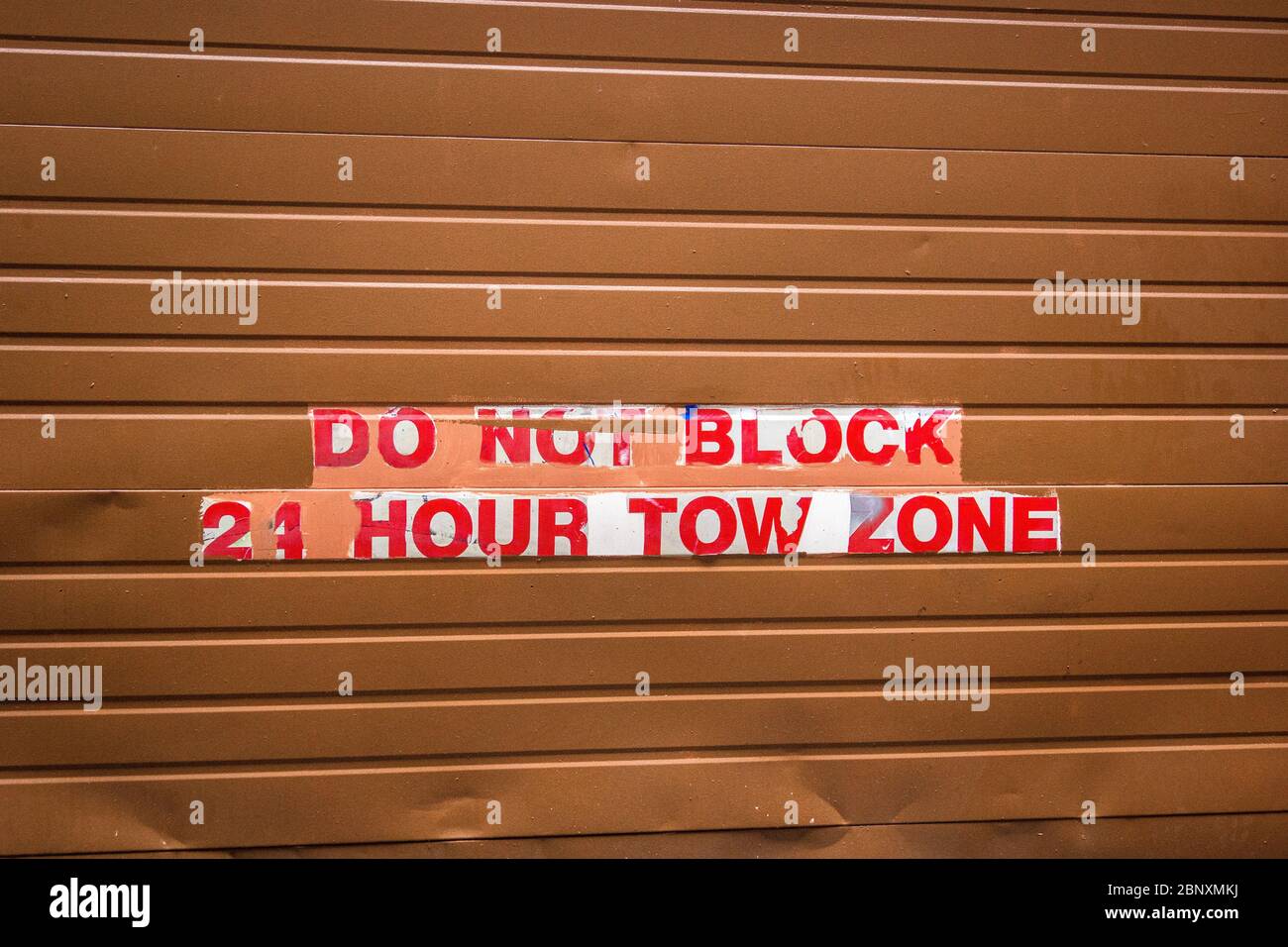 A metal roll up security door warning of a 24 hour tow zone. Stock Photo