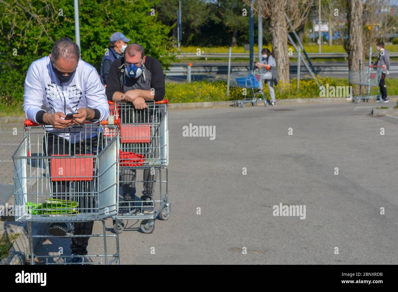 Closeup of group of tired italian white men wearing coronavirus protection masks. Line of people, shopping carts near grocery store fearing 2nd wave Stock Photo