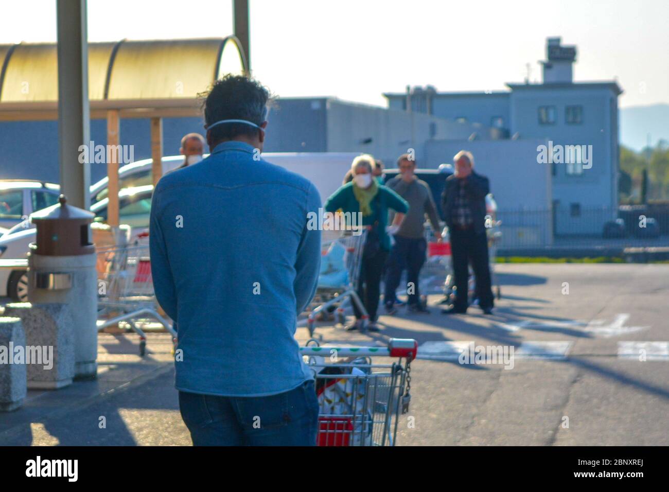 Symbolic scene from an italian grocery store during coronavirus pandemic: the back of a man with COVID-19 protective mask exiting with shopping cart Stock Photo