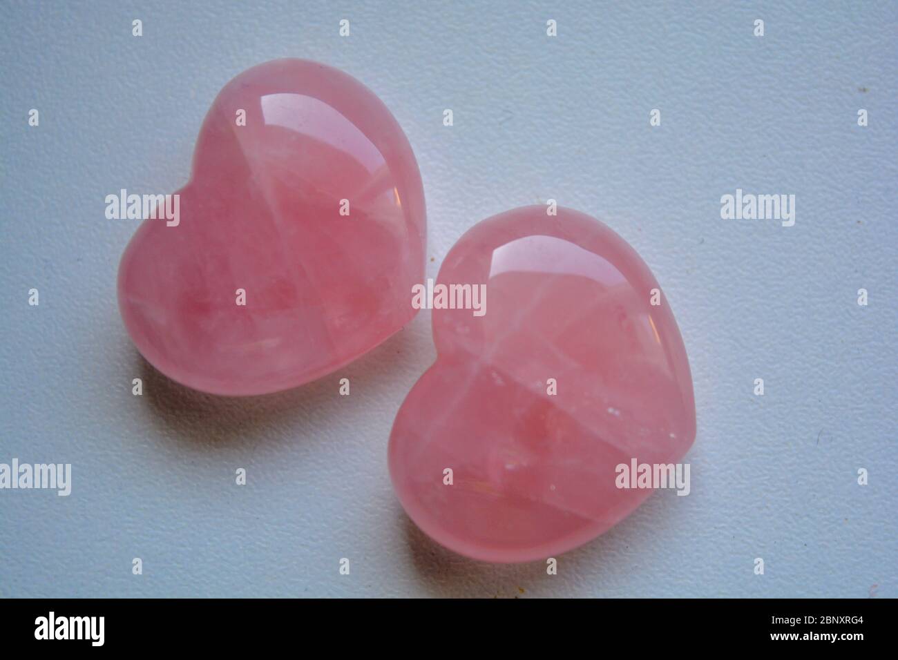 Two heart shaped semi-precious stones. Light pink quartz gems on a white background. Romantic carved minerals, precious stone gift Stock Photo
