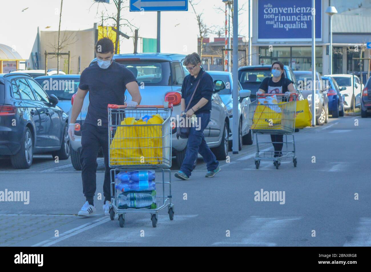 Three people walking in line, wearing coronavirus protection masks pushing shopping carts full of bags of groceries and essentials fearing second wave Stock Photo